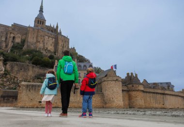 Heyecanlı çocuklar eski taş bir kalenin önünde ellerini kaldırırken Fransız bayrağı yukarıda dalgalanarak tarihi ve mirası sembolize ediyor.
