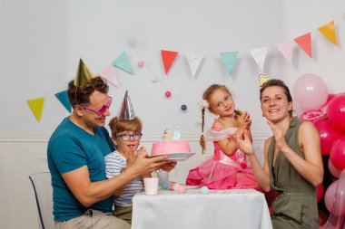 Mutlu bir ebeveyn, çocukların yanında oturup doğum gününü kutlar.