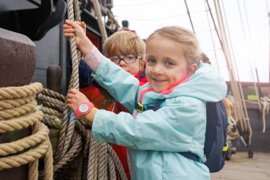 Neşeli çocuklar teknenin güvertesinde renkli ceketler giyip, güçlü bir halat çekiyorlar. Saint-Malo, Bretagne, Fransa 'da turistik yerleri ziyaret etmekten mutluluk duyuyorlar.