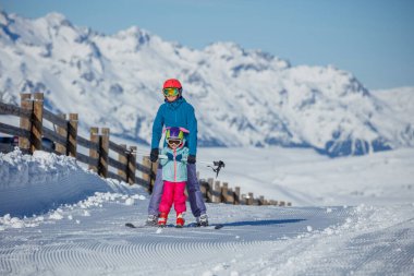 Yetişkin bir eğitmen ve bir çocuk birlikte yokuş yukarı kayarak, taze bir sabah karında çitli bir yolu takip ediyorlar.