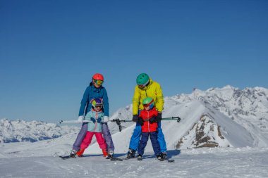 Dört kişilik bir aile, karla kaplı dağlara karşı birlikte kayak yapmaktan keyif alır.