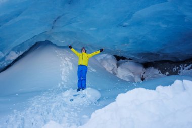 Genç yetişkin kayak yaparken buz kemeri altında parlak mavi bir buzul mağarasına hayran olmak için mola veriyor.