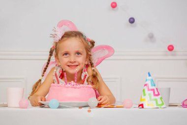 Pembe pasta ve renkli süslemelerle dolu bir partide neşeli bir çocuk.