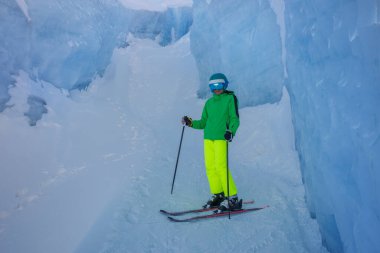 Yüksek buz duvarları arasında neon renkli manevra yapan bir kayakçı.