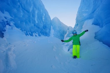 Göz kamaştırıcı buz oluşumlarının ortasında, parlak yeşil kıyafetli, neon kayak pantolonu ve kaskı olan bir kişi, kayak takımlarını buzlu zemine karşı çarpıcı bir kontrast oluşturuyor.