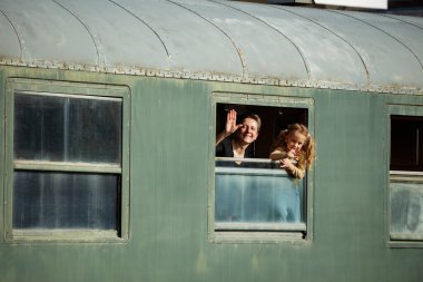 Anne ve kızı el sallıyor, yaz tatili boyunca trenle seyahat etmekten mutlu bir şekilde gülümsüyor.