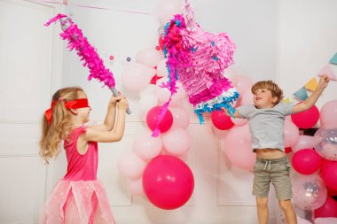 Rengarenk bayraklar ve balonlarla süslenmiş bir odada, gözleri bağlı bir prenses, kardeşinin tezahüratıyla tek boynuzlu at pinatasını parçalamaya çalışıyor.