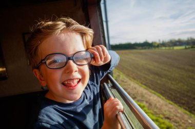 Çocuk pencerenin çerçevesini tutuyor, klasik tren ufuk çizgisine doğru süzülürken açık arazilerin bulanıklığına sessizce bakıyor.