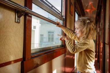 Komik kız, tren koridorunda dur. Pencereye bak. Gülümse ve bir şeyi işaret et.