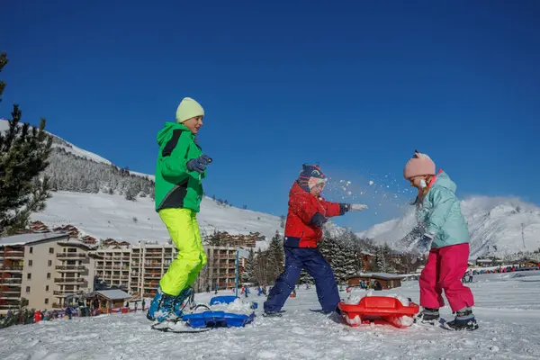 Çocukların aksiyon görüntüsü, iki erkek ve kız, kar savaşı yaparken, kış tatillerinde kayak merkezinde.