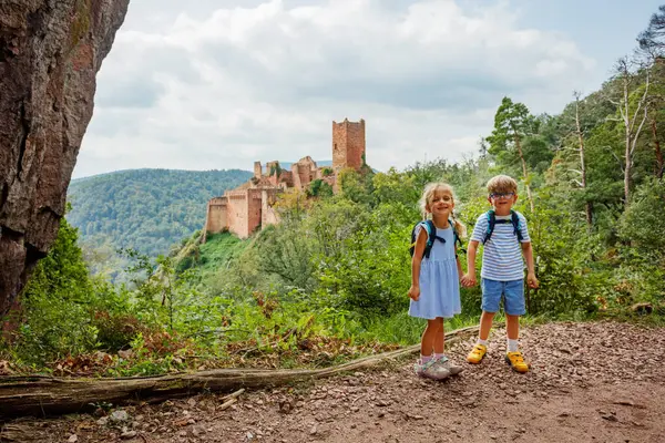 Tarihi bir kale Saint-Ulrich ve yeşil tepelerin önünde, sırt çantalı iki mutlu çocuk Avrupa 'da, Alsace bölgesinde, Fransa' da poz veriyor.