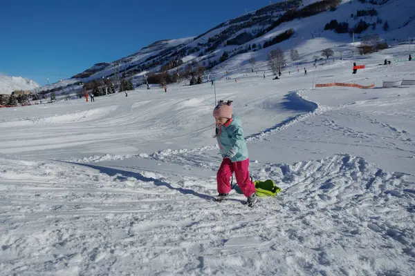 Bir çocuk, açık mavi bir gökyüzünün altında, Fransa 'da Noel tatillerinde neşeli bir şekilde kızağı sürüklüyor.