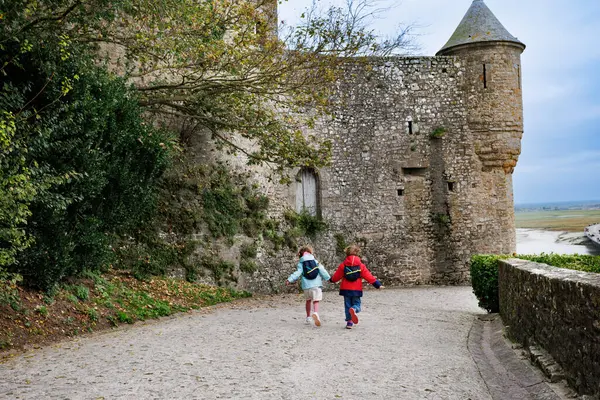 Ortaçağ kalesinin yanındaki kaldırım taşından yolda koşan bir çift çocuk, arka planda resim gibi bir manzaraya sahipler.