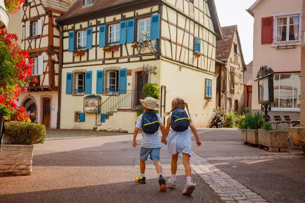 Sırt çantalarını taşıyan iki çocuk, Fransa 'nın Alsace bölgesinde Avrupa' da yarı keresteli geleneksel evleri olan pitoresk bir köyde dolaşıyorlar.