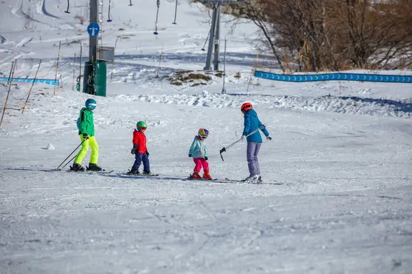 Kayak koçu renkli giyinmiş üç çocuğa koçluk yapıyor. Karla kaplı bir dağda teknikler gösteriyorlar.