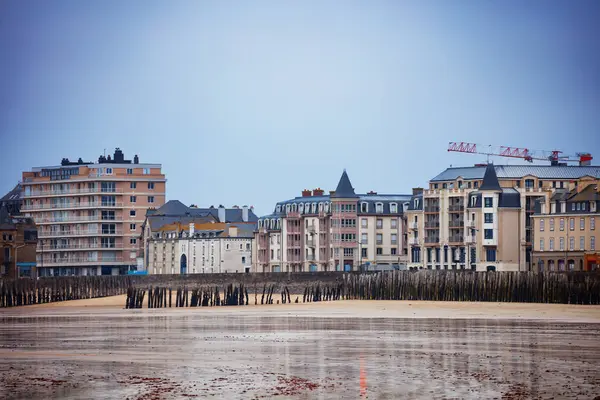 Sahil şeridi, önünde geniş bir kumlu alan ve bulutlu bir zemin, Saint-Malo, Bretagne, Fransa ile birlikte tarihi yapılarla işaretlenmiştir.