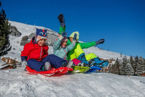 Üç çocuk karlı yamaçtan iniyor. Kış tatillerinde kayak merkezinde iyi eğlenceler.