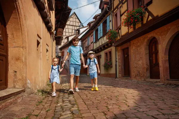 Çocuk gezginler Eguisheim, Avrupa, Alsace bölgesi, Fransa 'da karakteristik renkli evlerle dolu taşlarla döşenmiş bir caddede sakin bir yürüyüşün tadını çıkarıyorlar.