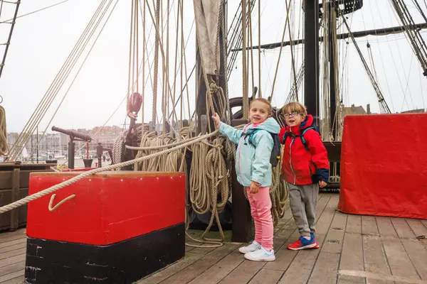 Okul gezisindeki iki çocuk, renkli ceketler ve sırt çantaları giymiş halatlarla çevrili bir gemi güvertesini keşfediyor. Saint-Malo Bretagne, Fransa