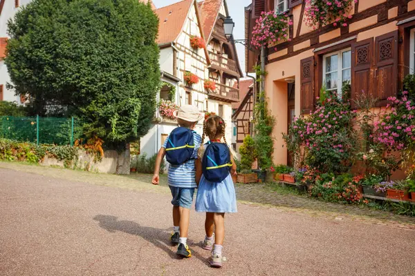 Sırt çantalı iki çocuk Fransa 'nın Alsace bölgesinde Avrupa' daki renkli ve tarihi binaların yanından geçen büyüleyici bir köyü keşfediyorlar.
