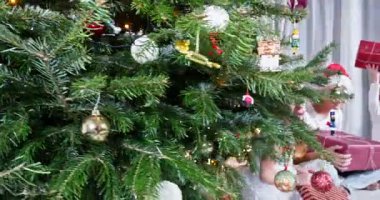 Konforlu oturma odasında, Noel Baba şapkalı üç genç güzel süslenmiş bir Noel ağacının yanında oturuyor, her biri hediyelerle dolu.