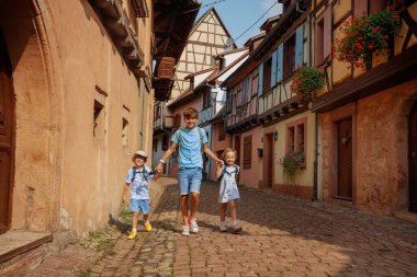 Çocuklar Avrupa 'da, Alsace bölgesinde, Fransa' da renkli ve kırsal binalarla çevrili büyüleyici bir kaldırım yolu boyunca birlikte yürüyorlar.
