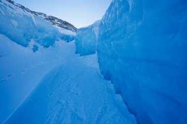 Açık bir gökyüzü ve arka planda dağ altında yüksek mavi buz duvarlarıyla çevrili dar bir geçit.