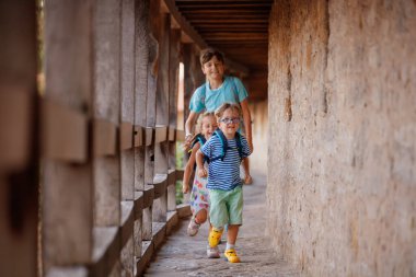 Üç çocuk, sırt çantalı turistler Rothenburg ob der Tauber, Almanya, Bavyera 'da duvarın taş geçidi boyunca yürüyorlar.