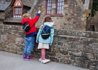 Sırt çantaları takan iki çocuk, bir çocuğun işaret ettiği gibi bir taş bina tarafından büyülenir.