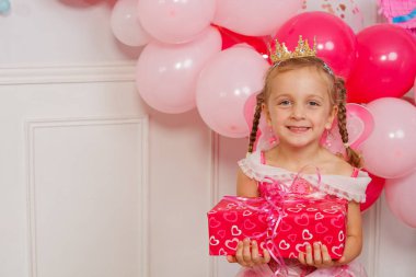 Peri gibi giyinmiş neşeli bir kız, bir şenlik vesilesiyle pembe ve altın balonların arasında gülüyor.