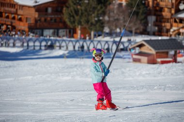 Kışın giyinmiş genç bir kayakçı, karlı bir Alp otelinde kaldırma ipine tutunuyor.