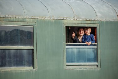 Anne ve çocuk pencerenin önünde dikiliyor, manzarayı parmaklarıyla görüyor, yaz tatillerinde trenle seyahat etmekten mutlu oluyorlar.