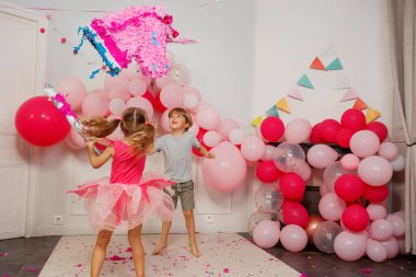 Şenlikli bir odada, gözleri bağlı prenses elbiseli bir çocuk, kardeşi tarafından cesaretlendirilen tek boynuzlu at pinatasına yumruk sallıyor.