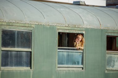 Yeşil vagon pencereli küçük bir kız dışarı eğiliyor, heyecanlı bir şekilde bakıyor, yaz tatili boyunca trenle seyahat etmekten mutlu.