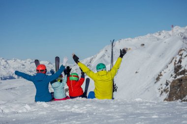 Karlı bir zirvede, renkli giyinmiş bir kayakçı ailesi uzak, karlı zirvelerde tatillerini kutlamak için ellerini kaldırdılar.