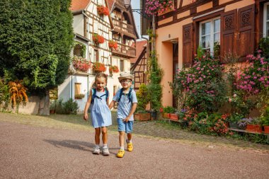 Sırt çantalı iki genç gezgin Avrupa, Alsace bölgesi, Fransa 'daki Eguisheim kasabasının kaldırım taşı sokaklarında maceralı bir yürüyüş yapıyorlar.