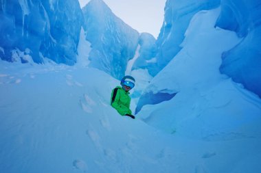 Muazzam buzlu duvarların içinde oturan bir genç neon giysi ve kayak kaskı takıyor.