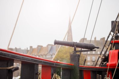 Saint Malo şehir zeminine bakan eski bir gemi topunun yakın plan çekimi, silaha odaklanmış ve uzaktaki bulanık binalar