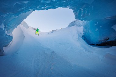 Donmuş bir tünelde süzülen kayakçı yeşil ceketli ve sarı pantolonlu.