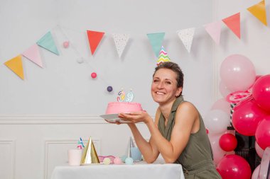 Balon ve kiraz kuşlarıyla dolu bir festival odasında, bir kadın doğum günü pastası tutmaktan mutluluk duyar.