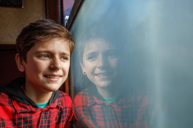 Pencere, yaz tatili boyunca kırmızı kareli bir bluz giyen bir çocuğun gülümsemesini yansıtıyor.