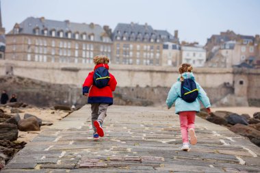 Bir çift çocuk sevinçle kaldırım boyunca koşuyor tarihi mimarisi ve arkadaki kayalık sahili ile Saint-Malo, Bretagne, Fransa