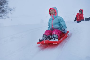 Kırmızı bir kızakla kayan bir çocuk dik bir tepeden aşağı kayıyor yüksek dağ zirveleri tarafından çerçevelenmiş, çocuk sadece kızağını itti.