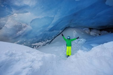 Karlı arazinin ortasında, gökyüzü mavisi buzdan bir mağarada renkli giyinmiş genç bir kayakçı duruyordu.