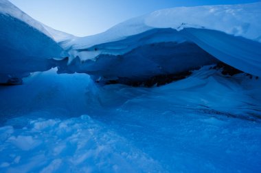 Karmaşık buz mağarası oluşumlarına sahip buzullar, berrak ve canlı bir gökyüzünün arka planına kurulmuş.