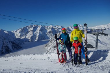 Renkli miğferler ve kayak kıyafetleriyle bu dört kişilik aile, karla kaplı dağ yamacında güneşli bir günün tadını çıkarıyor.