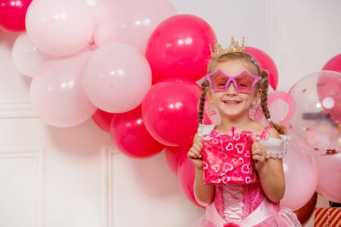 Pembe balonların ortasında parlak, yıldız şeklinde güneş gözlüklü ve altın bir taç takan genç bir prenses mutlu bir şekilde doğum gününü kutluyor.