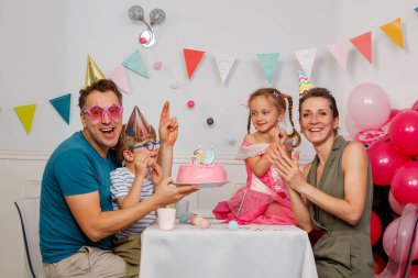 Arka planda renkli balonlar ile, mutlu bir aile mum kaplı bir pasta etrafında güzel bir doğum günü anı paylaşıyor.