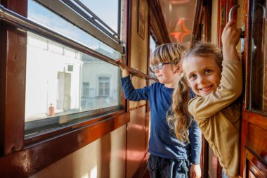 Mutlu kardeşler, erkek, kız retro tren vagonunda gezerler, pencereden dışarı bakarlar ve kapılara asılırlar.