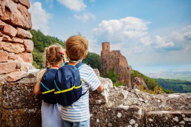 Bir oğlan ve kız sırt çantalarını takmış taş duvarda duruyorlar. Fransa 'nın uzak bir köşkündeki Girsberg Kalesi' nin kalıntılarına hayran bakıyorlar.